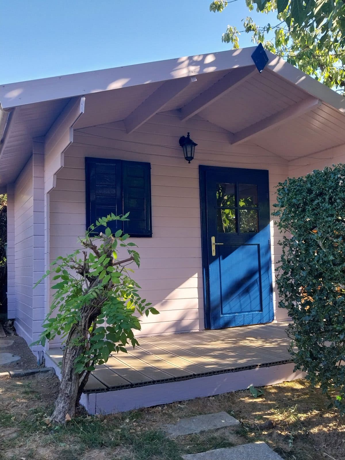 Façade d'un chalet de jardin repeinte en blanc rosé, porte et volet en bleu nuit