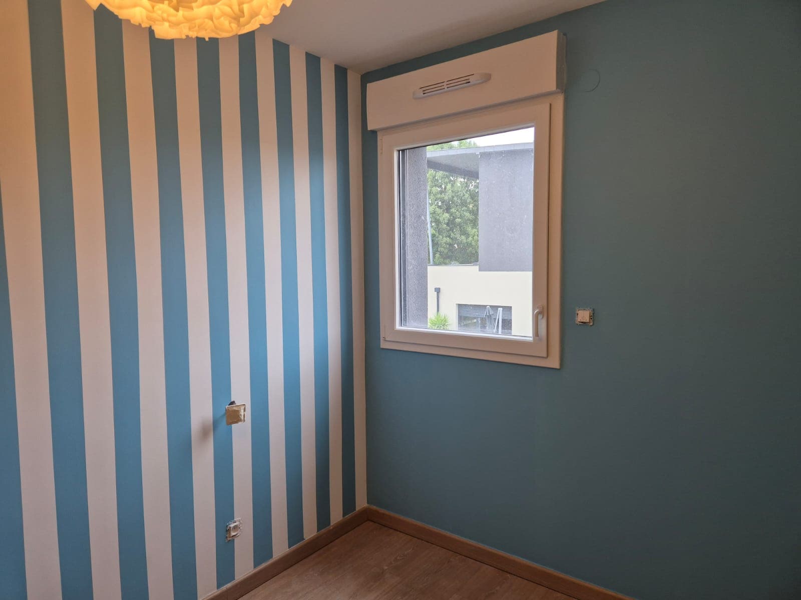 Chambre d'enfant : un mur à rayures verticales bleu canard et blanc, le mur voisin uni dans le même bleu